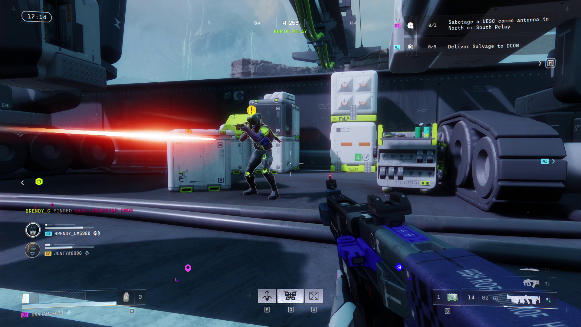 A robot stands and fires a gun next to some boxes.