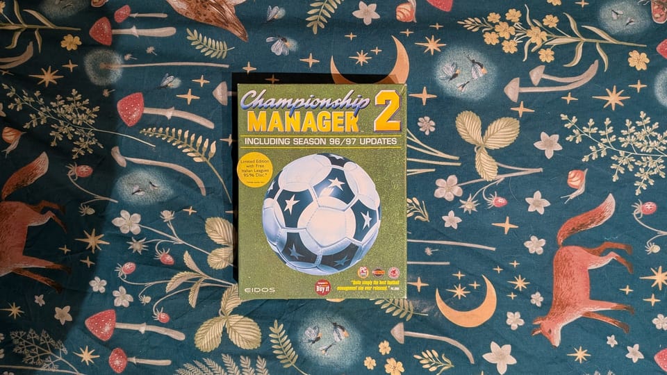 A boxed copy of Champion Manager 2 on a bed spread. There are creases and dog hair everywhere.